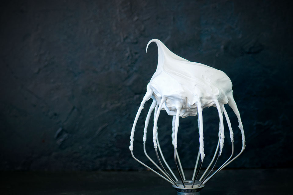 Whipped egg whites - beaten italian merengue on a whisk on black