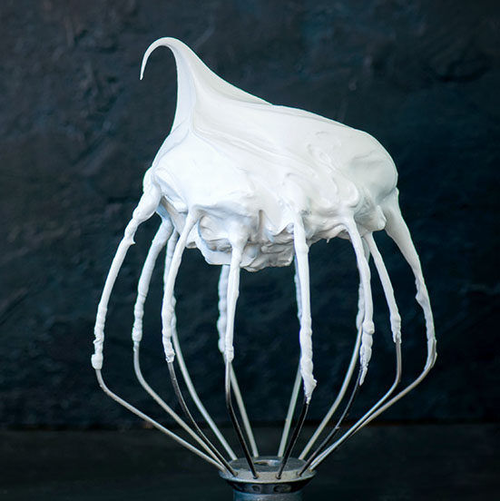 Whipped egg whites – beaten italian merengue on a whisk on black