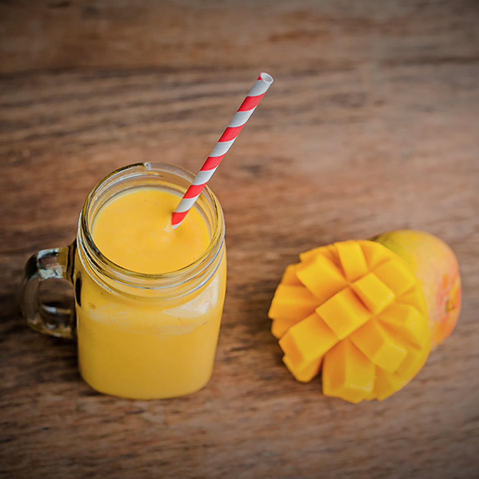 Juicy smoothie from mango in glass mason jar with striped red straw on old wooden background. Healthy life concept, copy space